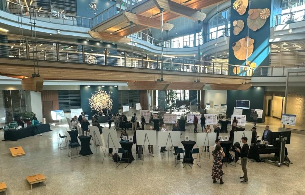People gather in a large atrium with scientific posters and table displays.